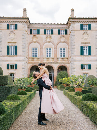 Groom picks up Bride wearing pink designer gown standing in front of Villa Cetinale in Tuscany, Italy
