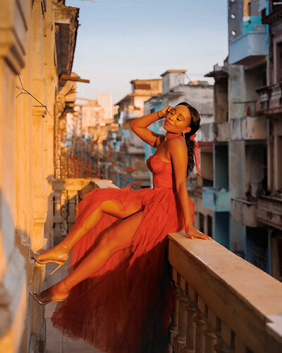 Woman sits on a balcony railing in a rust-colored gown