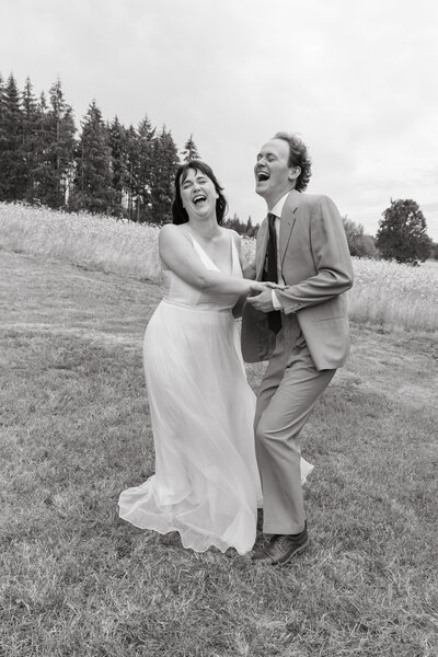 Black and white image of an couple holding hands and laughing on their elopement day.