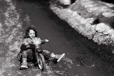 Child rides toy motorcycle down path with snow piles, winter family moment in Breckenridge.