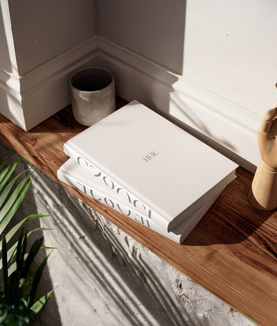 White books with luxury packaging arranged on wooden surface with soft natural lighting and plant decor.