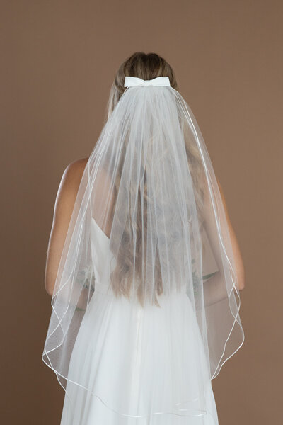 Bride wearing a two layer fingertip length veil with ribbon edge, and holding a white and blush bouquet