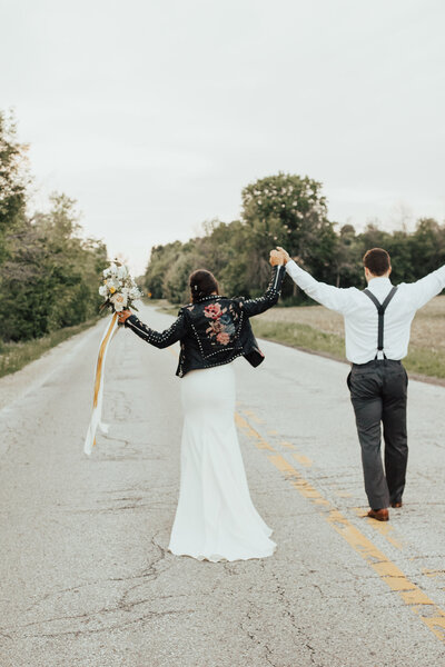 Bride and groom walking down a road with hands up in celebration of their marriage