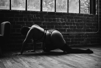 artistic photo of  a black woman crawling across a hardwood floor wihile light illuminates her from above in a boudoir studio