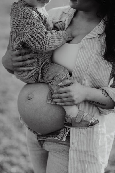 Close up of pregnant belly with toddler sitting on top.