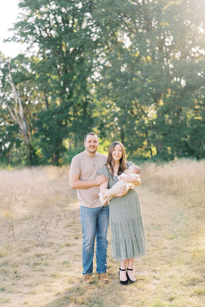family of three in a sunlit field during outdoor newborn photos