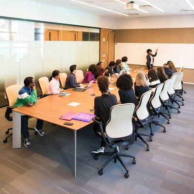 Group of people seated around a large conference table listening to a presenter.
