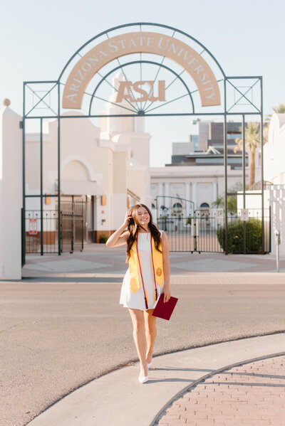 Senior girl holding her grad cap and playing with her hair while walking and smiling