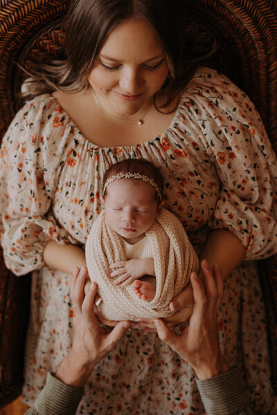 Sweet newborn baby girl in a yellow outfit and flower crown wrapped in a floral blanket.
