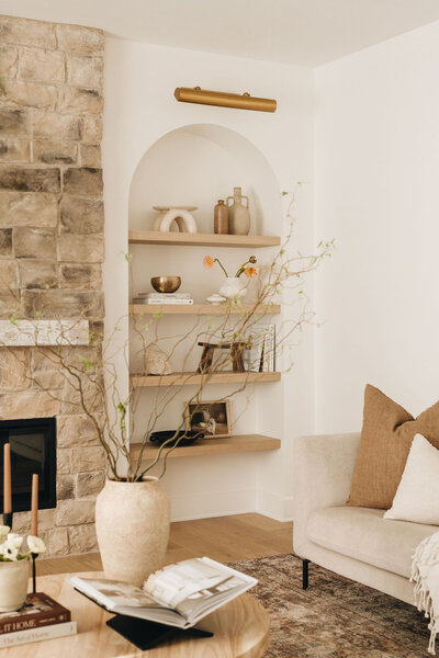 Arched built-in shelves styled with neutral ceramics and books beside a stone fireplace in a modern Montreal living room – by Ingrid Interior Design.