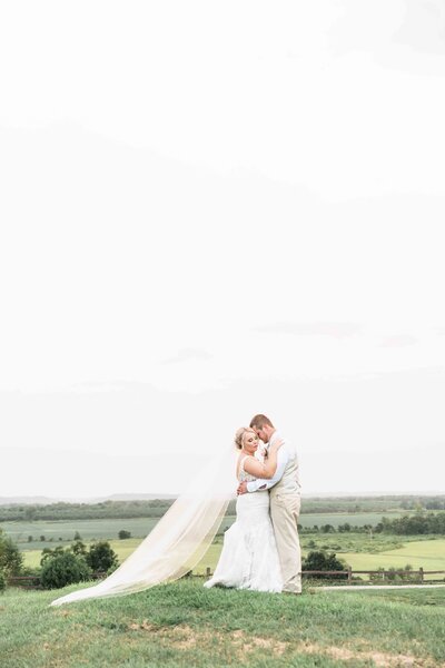 bride and groom hugging in field with giant viel