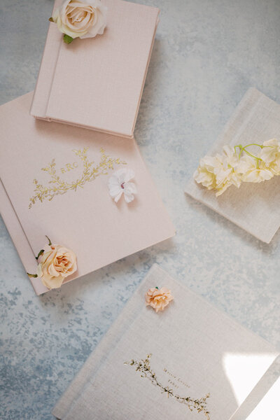 Light pink maternity photo album lay on a blue backdrop with florals.