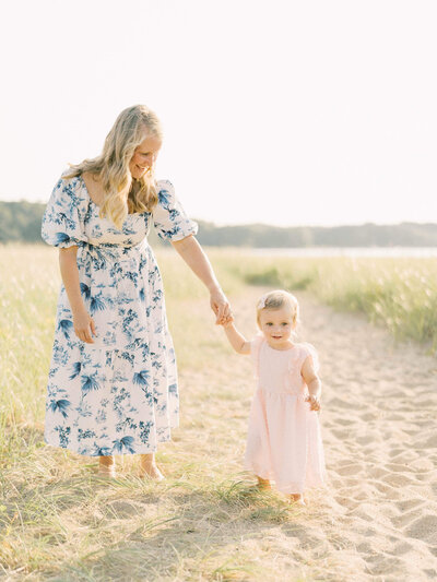 mother helping daughter learn to walk on the beach By Carrie Pellerin