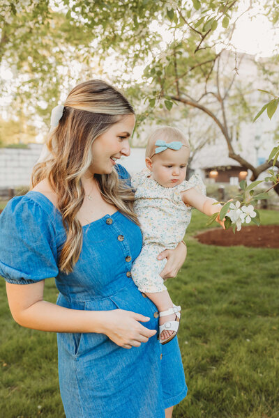 mom holds little girl as she checks out the flowers on a blooming tree