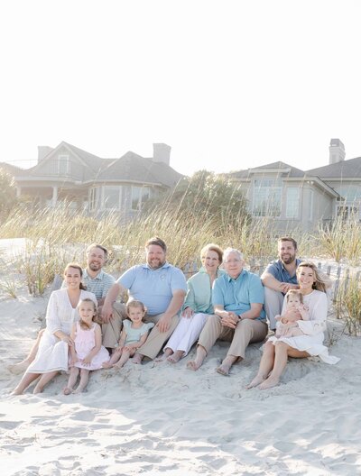 A Hilton Head extended family of ten sits on the beach during golden hour for a family portrait, captured by a Hilton Head photographer, Lamp and Light Photography.