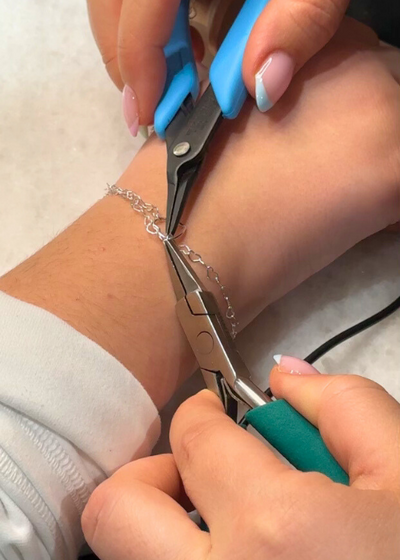 Permanent bracelet welding in progress on wrist with gold chains.