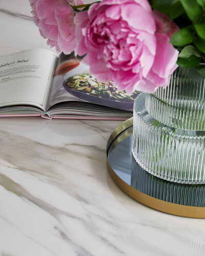 A vase of pink flowers and a cook book sitting atop a marble countertop