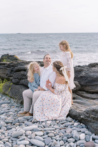Richmond Family Photographer | Jacqueline Aimee Photo of a family of four sits together on a rocky cliff with the ocean behind