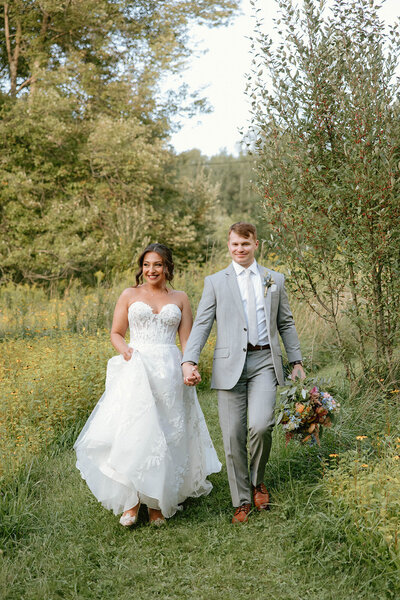 Bride and groom holding hands walking through a grassy field