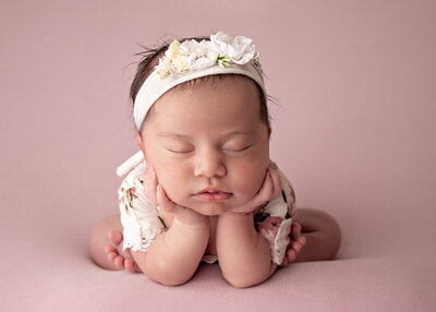 Newborn girl on a soft pink backdrop and floral attire.