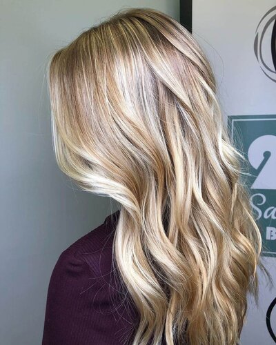 A side view of a woman with sleek, wavy blonde hair, showcasing a beautifully styled look by 212 Salon, Spa, & Barbershop.