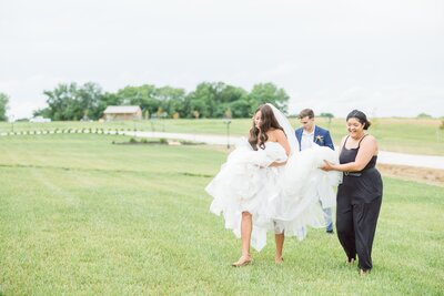 Wedding planner helps bride carry dress  through the grass at the English Barn Wedding Venue