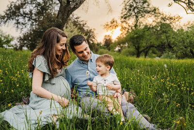 pregnant couple with toddler boy sit in a field of flowers