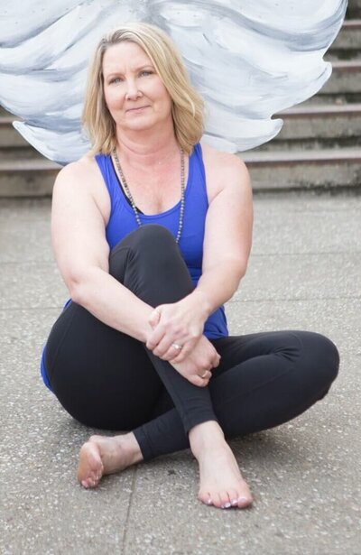 Susan sitting on the ground posing for a photo with soft white wings behind her.