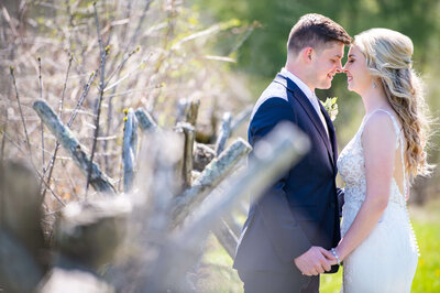 Ottawa wedding photography of a bride and groom  kissing along a rustic fence at Stonefields Estate taken by Ottawa wedding photographer JEMMAN Photography