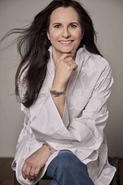 Silke, wellness coach for high-achieving women in midlife, smiling confidently in a white blouse with long dark hair flowing over her shoulder.