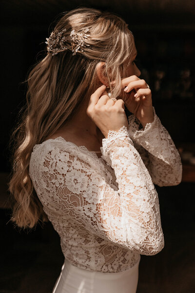 Bruid met een witte jurk in zacht licht doet oorbellen in. 