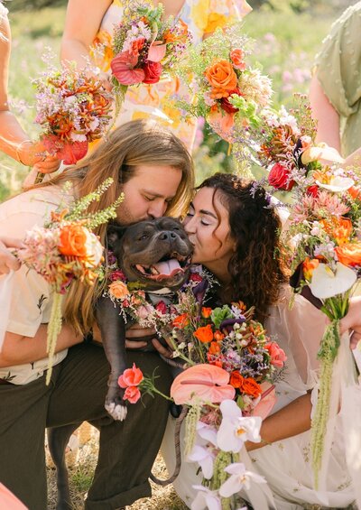 Colorful florals surrounding a bride and groom kissing their dog during their mountain elopement 