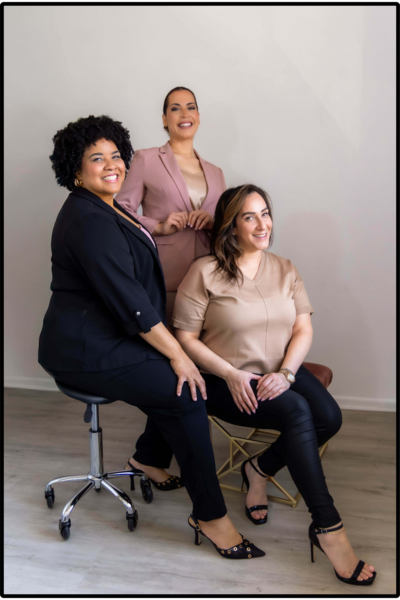 photo of 3 women - 2 women sitting in chairs and one standing, all smiling at the camera