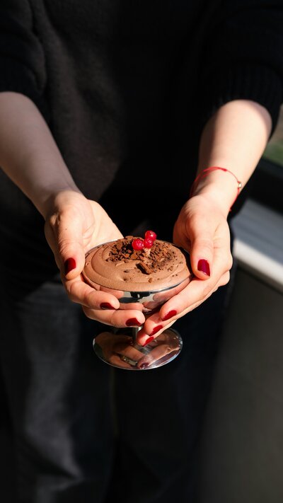 Hands holding a chocolate dessert in a silver dish