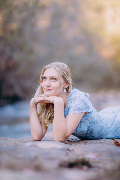 Whimsical senior portrait of a girl lying on the rocks on the bank of Line Creek in Peachtree City Georgia
