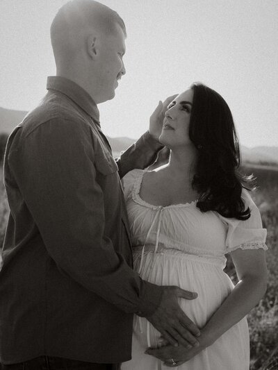 Pregnant woman standing in a field with mountains in the background, photographed in black and white.