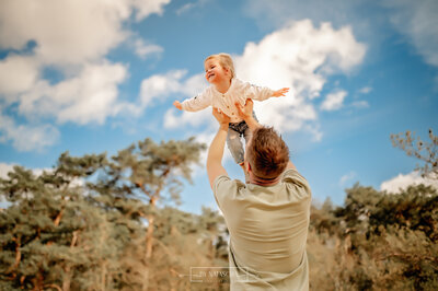 Papa gooit zijn armen in de lucht terwijl hij zijn dochter vasthoudt en haar laat vliegen in de lucht, waarbij ze haar armen gespreid houdt als een vliegtuig bij Herperduin