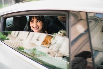 bride sits in the car looking out the window smiling