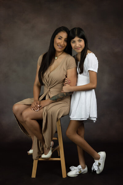 mom-and-daughter-wearing-tans-and-white-against-brown-backdrop-in-arlington-tx-studio