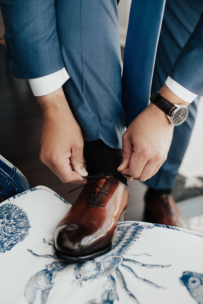 Groom tying dark brown leather shoes with one foot on ottoman