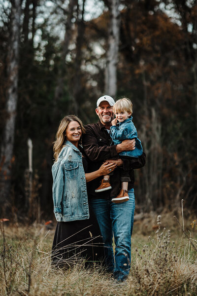 Young family smiling for photo in beautiful Wisconsin woods during fall.