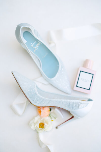 Flatlay of white lace heels with flowers and pink perfume bottle