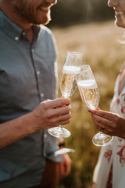 Couple toasts champagne flutes at sunset in a golden Breckenridge meadow for their engagement celebration.