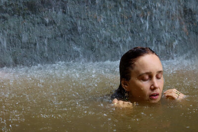 A portrait of a woman with her eyes closed basking under a waterfall in Bali, an example of Courtney's portraiture, retreat and event photography