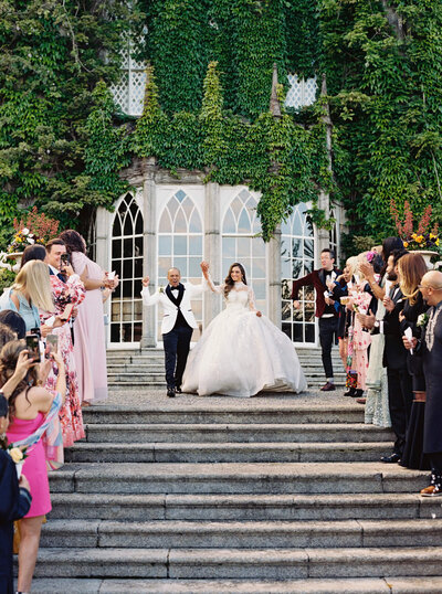 Newly wed couple holding hands in the air as people celebrate their marraige as they walk down the stone steps in front of them outside Luttrellstown Castle