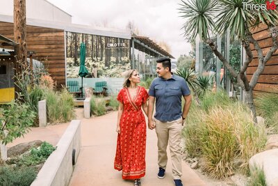 Engaged couple walk through The CAMP in Costa Mesa holding hands during photo shoot