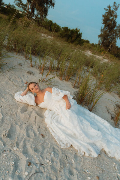 a woman in a wedding dress laying on the sand