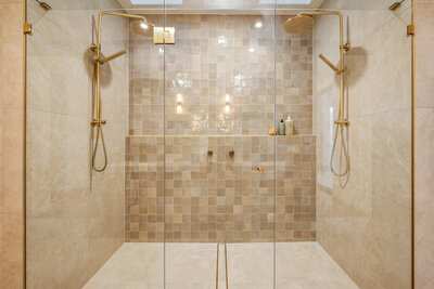 A luxurious double walk-in shower in the Marisol home, featuring warm textured tiles and brushed gold tapware.