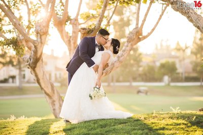 Groom dips and kisses his Bride under a tree at a golf course