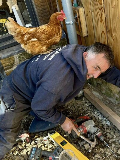Man working on the ground with a chicken standing on his back.